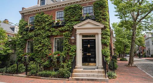 Exquisite Georgetown Federal townhouse exterior in Washington DC with black lacquered door, polished brass knocker, ivy covered brick facade, and manicured wrought iron window boxes